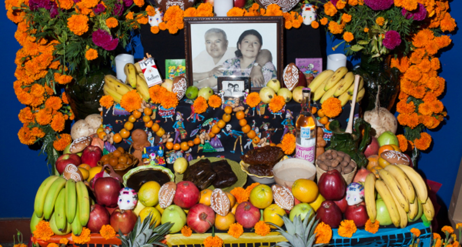 A Dia de los Muertos altar filled with food, dedicated to the dead people whose photographs are on the altar, framed