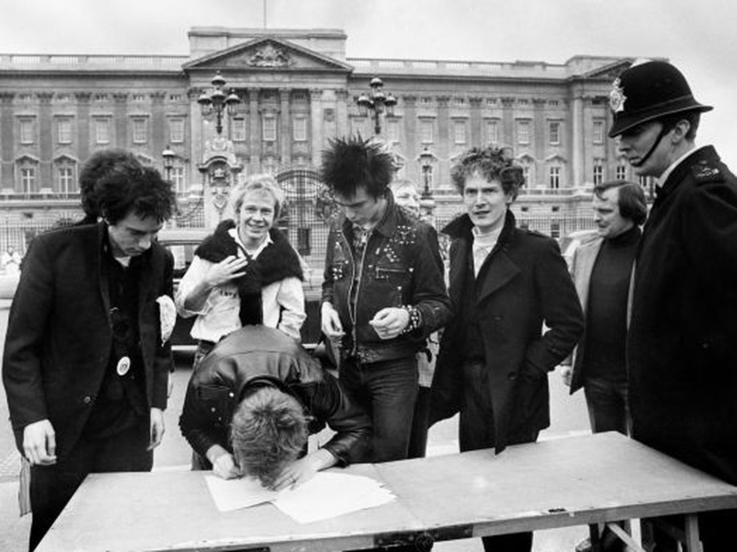 Τα μέλη των Sex Pistols υπογράφουν το συμβόλαιό τους με την EMI για το Never Mind The Bollocks έξω από το Buckingham Palace, υπό την επίβλεψη αστυνομικού
