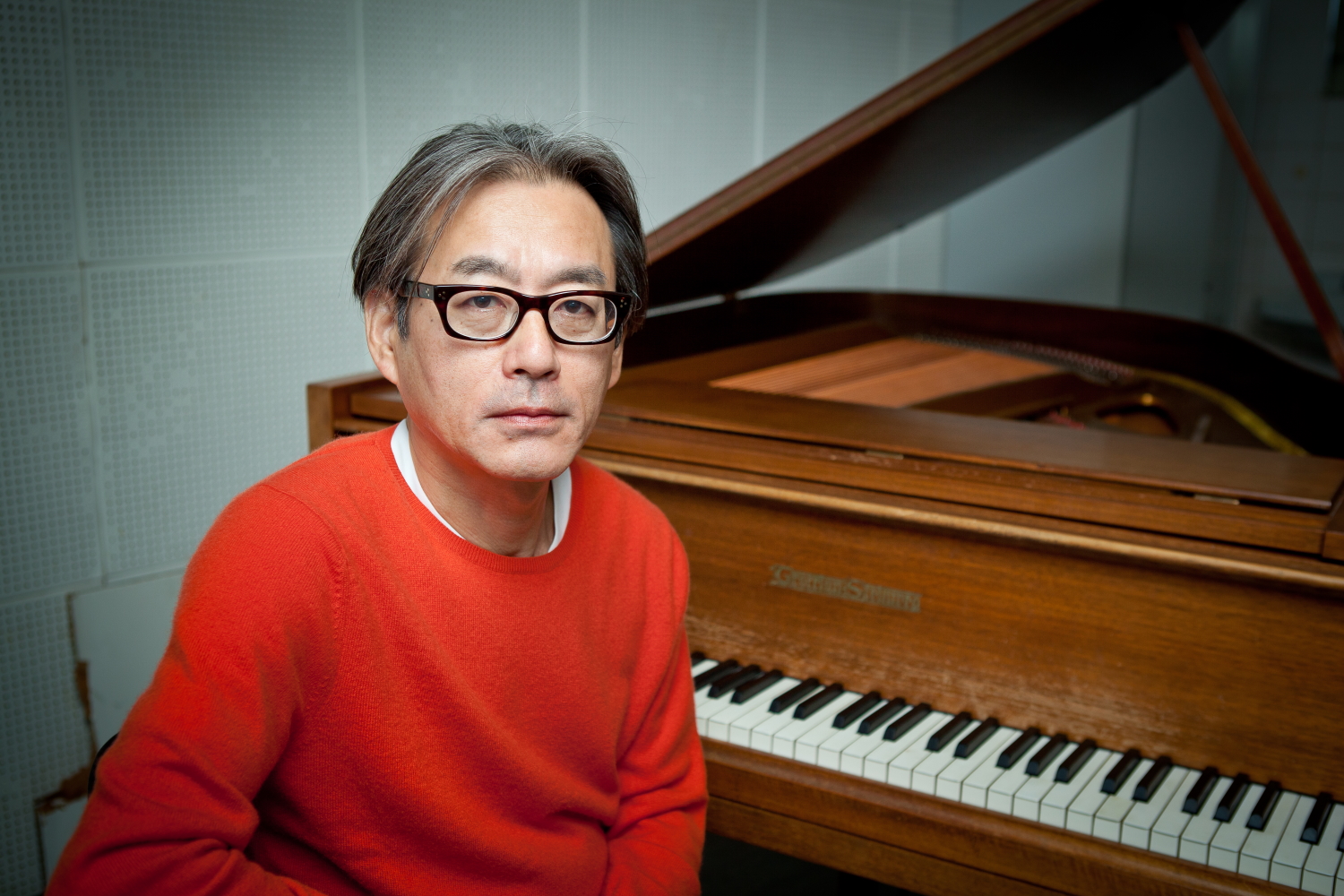 Japanese composer Shigeru Umebayashi posing for a photoshoot in front of his piano